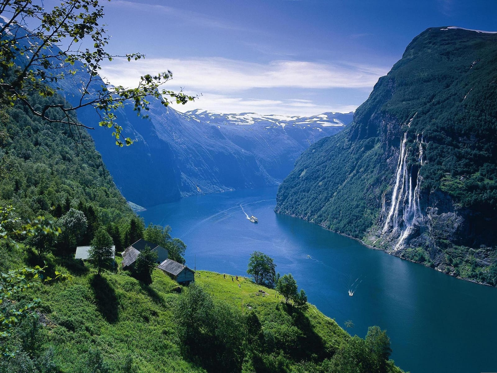 Fjord with waterfalls, boat and hillside cabins