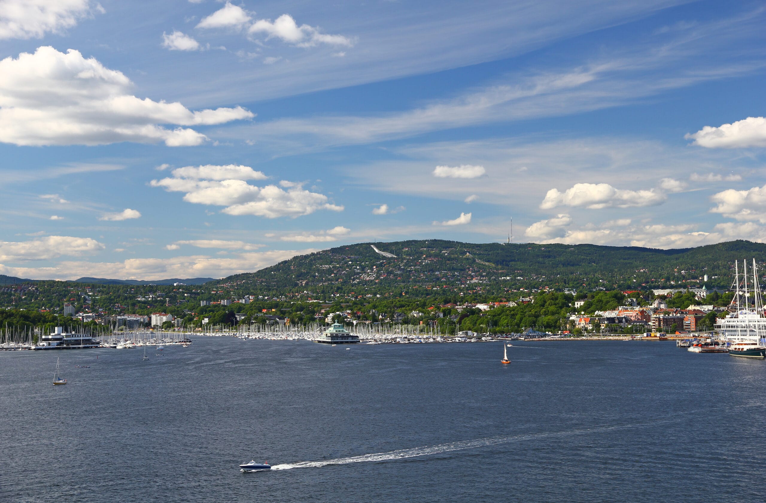 Waterfront city with marina and forested hills beyond
